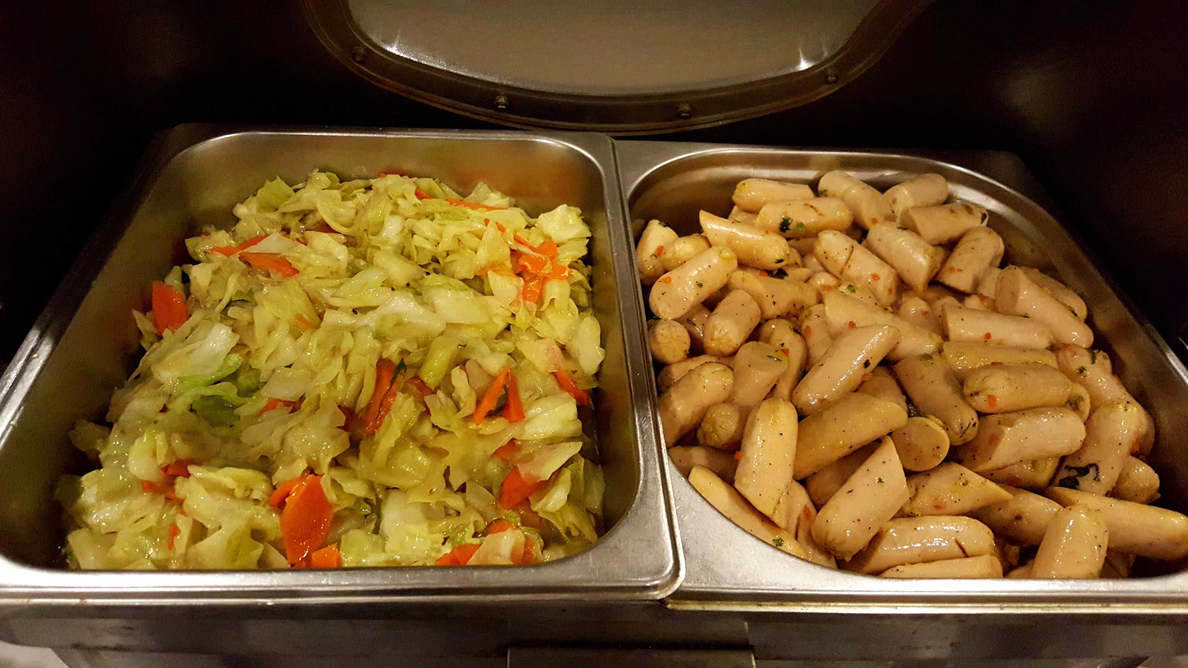 A buffet with two metal trays, one containing a vegetable salad and the other containing roasted potatoes.