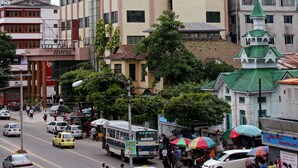 Un hotel de varios pisos con un letrero llamativo, una calle concurrida con vehículos y peatones, y edificios circundantes.