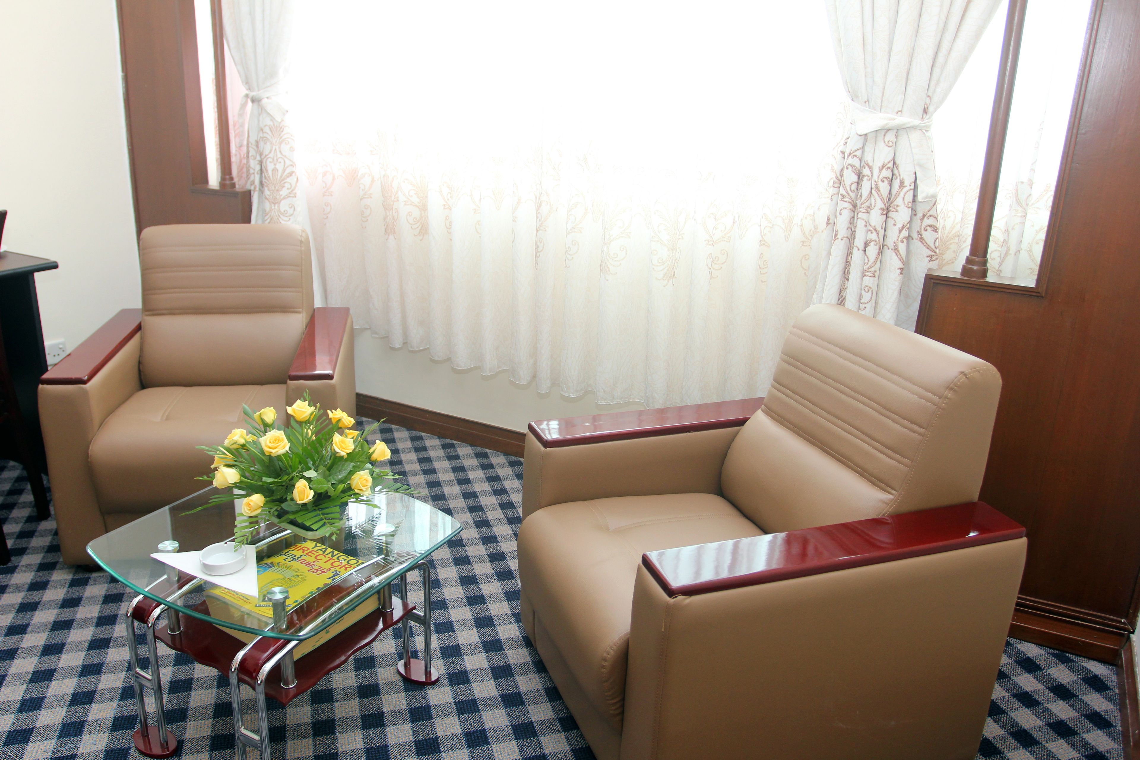 Ein Zimmer mit zwei beigefarbenen Sessel, einem Glastisch mit Buch und Blumen sowie einem karierten Boden.
