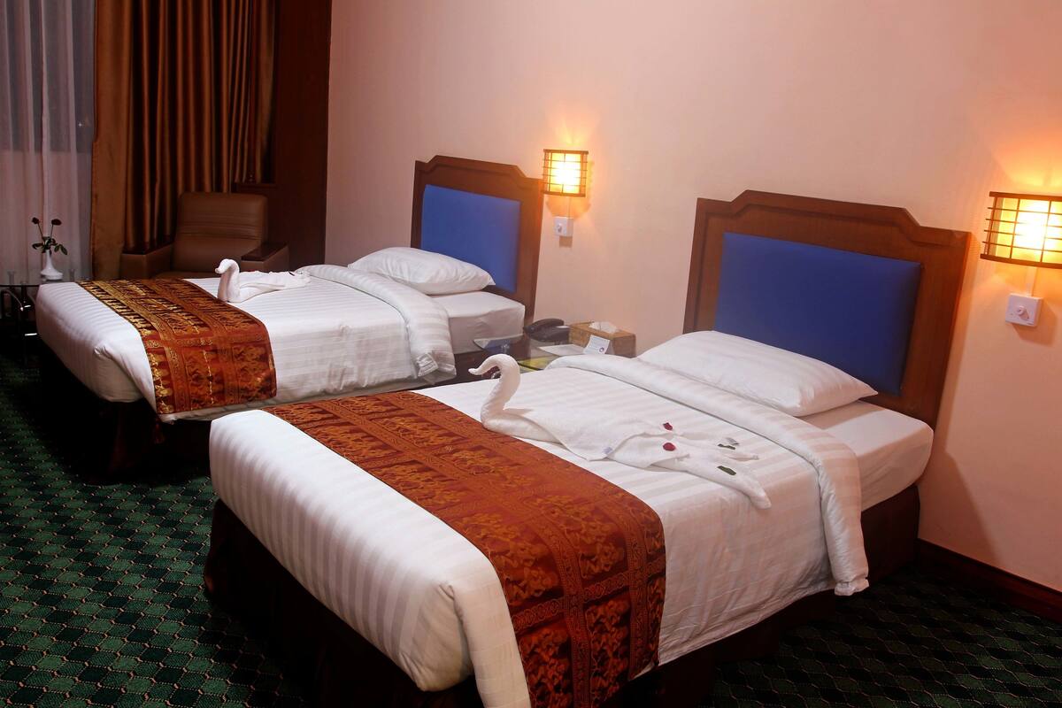Une chambre d’hôtel avec deux lits, chacun doté d’une tête de lit, d’une table de chevet et d’une lampe.
