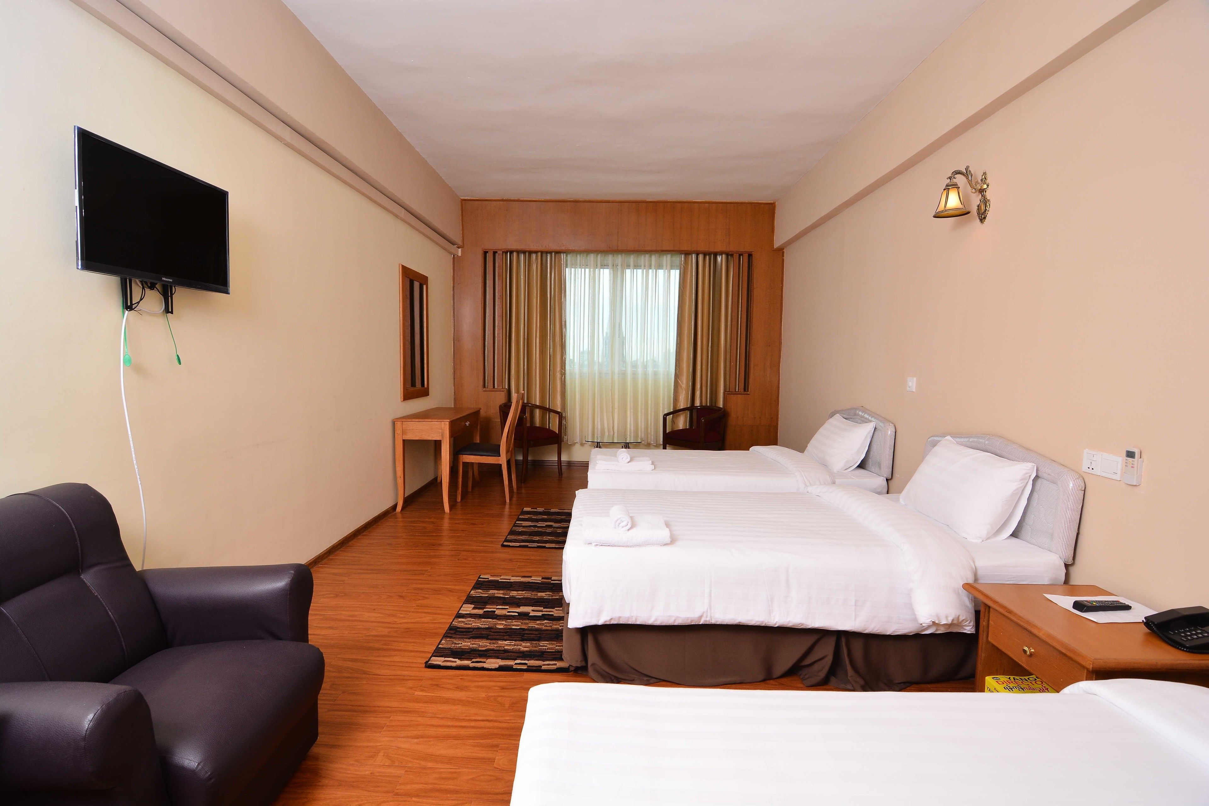 A hotel room with two beds, a desk, a chair, a television, and a wall-mounted light fixture.