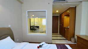 Habitación de hotel con cama, ventana, espejo, armario de madera y baño visible a través de la ventana.