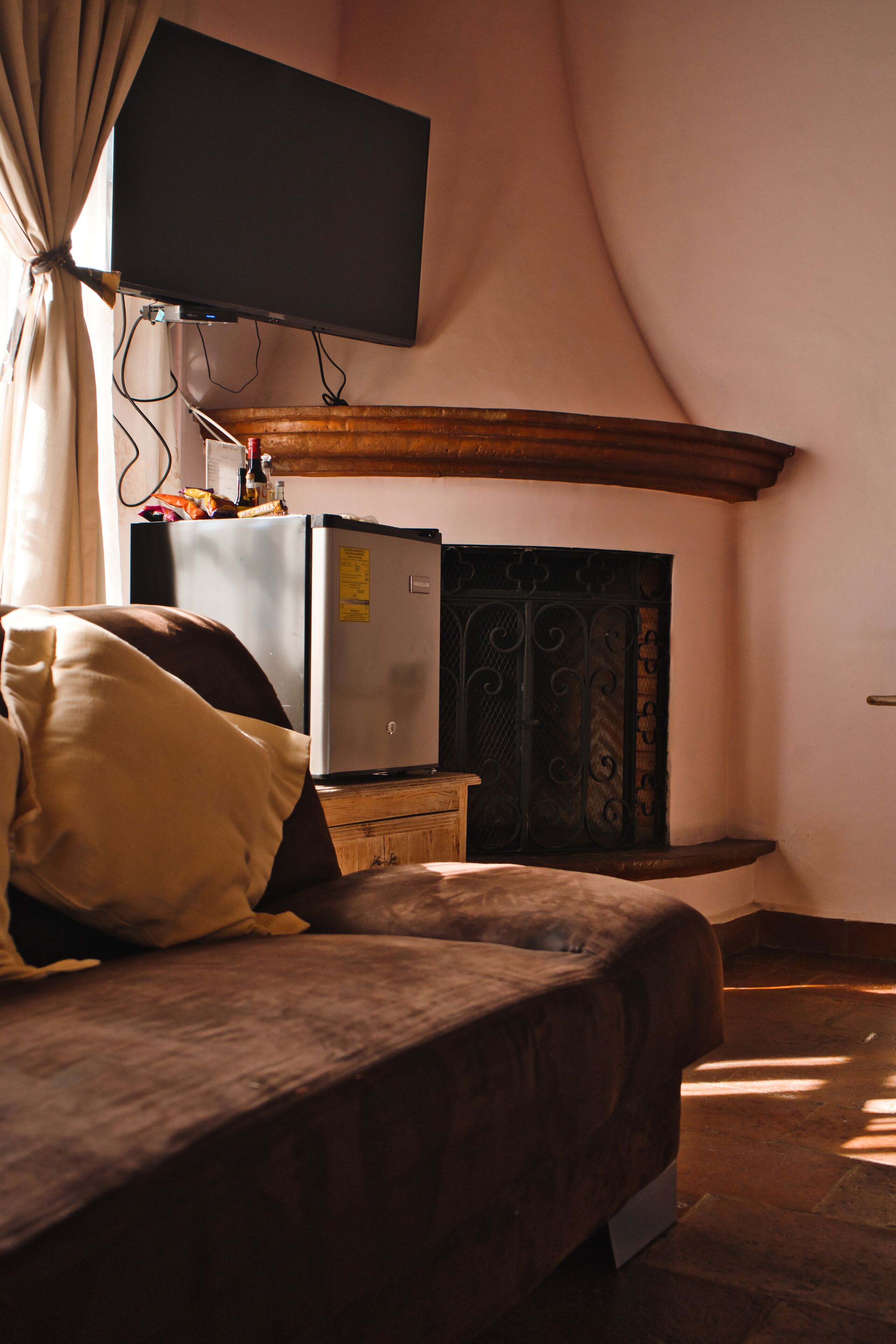 A bedroom with a bed, a television mounted on the wall, a refrigerator, and a decorative metal door.