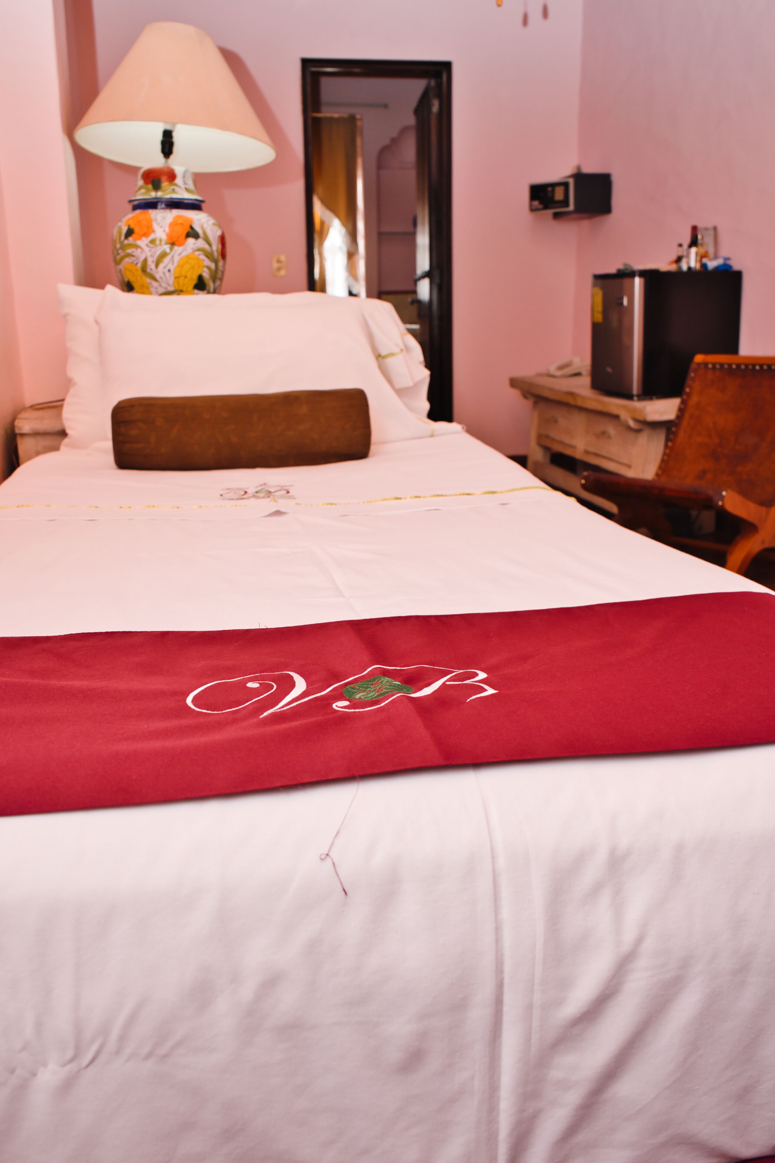 Una habitación de hotel con cama, lámpara, silla, escritorio y televisor.