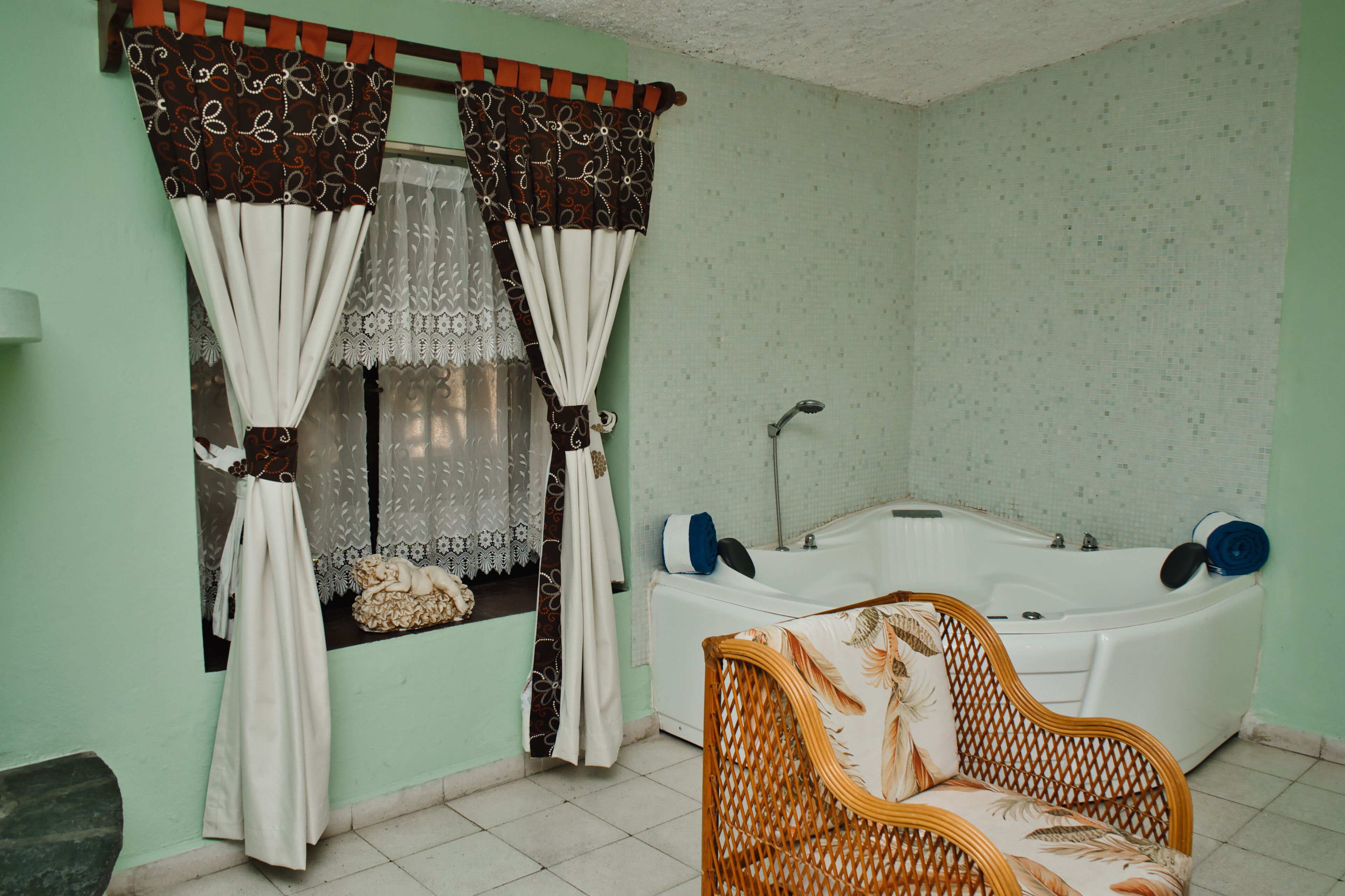 Une salle de bain avec une baignoire, un fauteuil en osier et une fenêtre avec des rideaux.