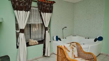 Une salle de bain avec une baignoire, un fauteuil en osier et une fenêtre avec des rideaux.
