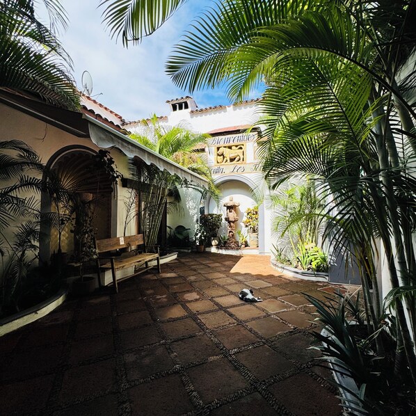 A courtyard with a tiled floor, palm trees, a bench, and a sign reading "Bienvenidos".