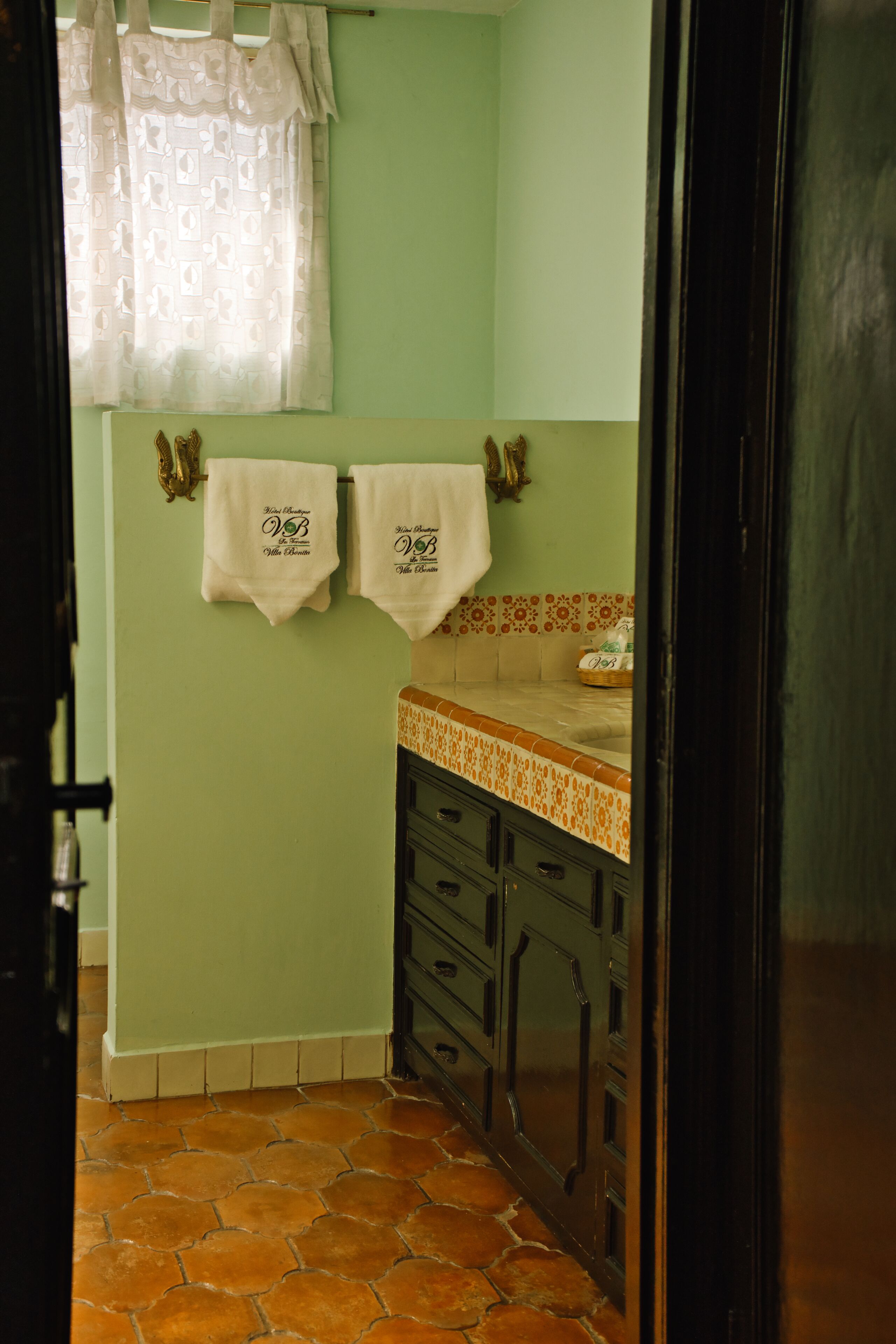 Un baño con paredes verdes, piso de baldosas y dos toallas colgadas en un perchero.