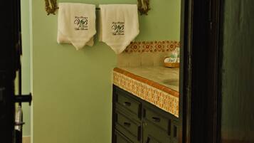 Un baño con paredes verdes, piso de baldosas y dos toallas colgadas en un perchero.