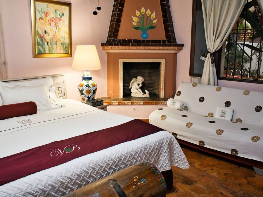 Un dormitorio con cama, sofá, chimenea y ventana con cortinas.