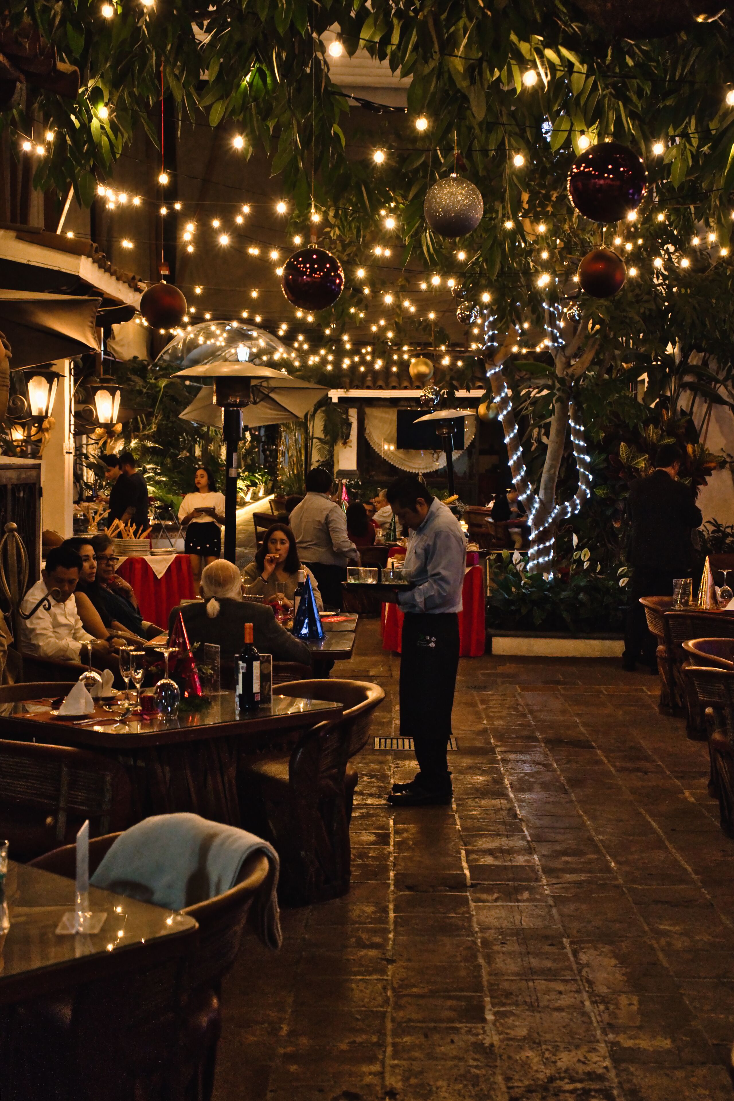 Un espacio de comedor al aire libre con mesas y sillas, luces colgantes y adornos.