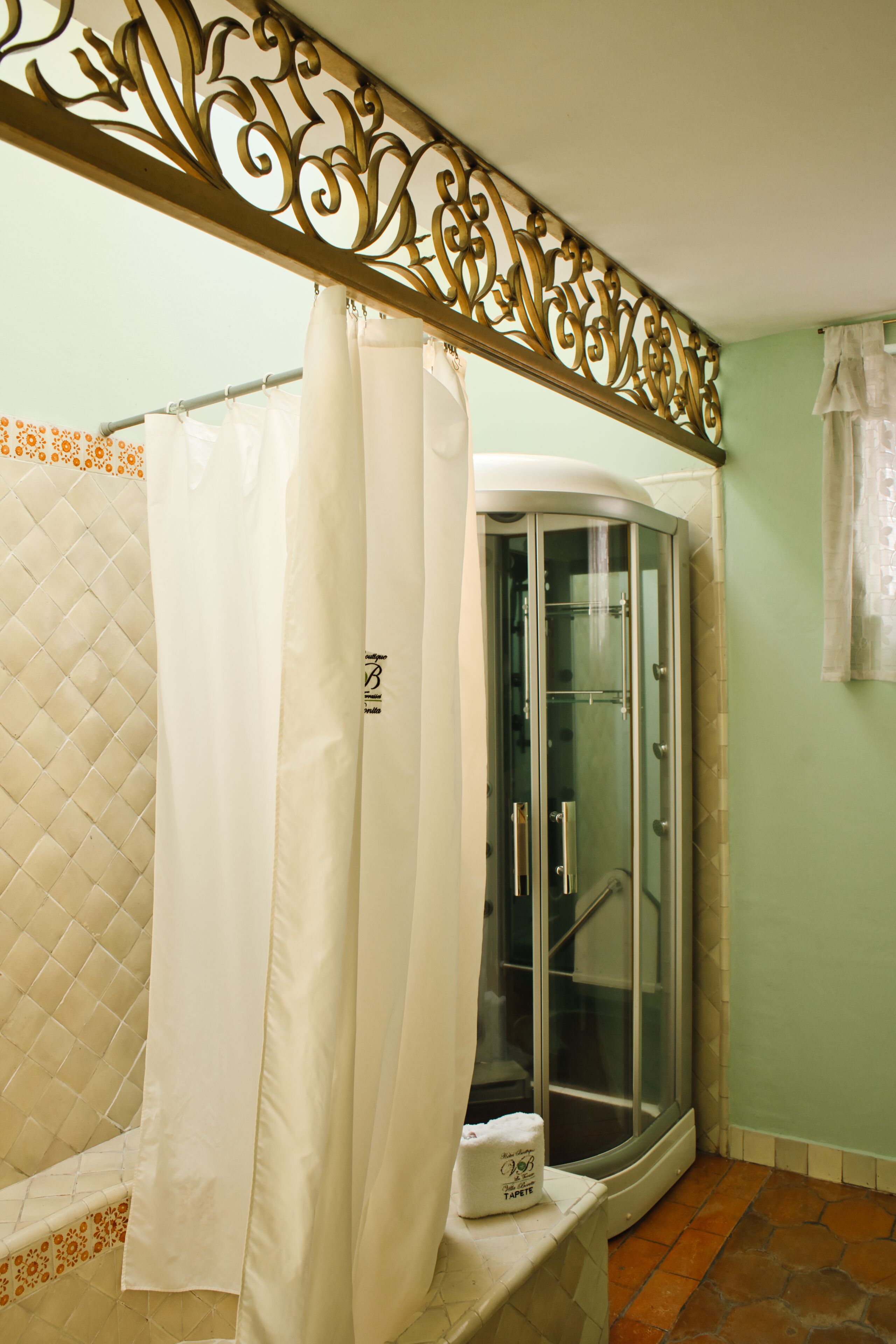 A bathroom with a glass shower enclosure, a white bathtub with a quilted pattern, and a decorative metal partition.
