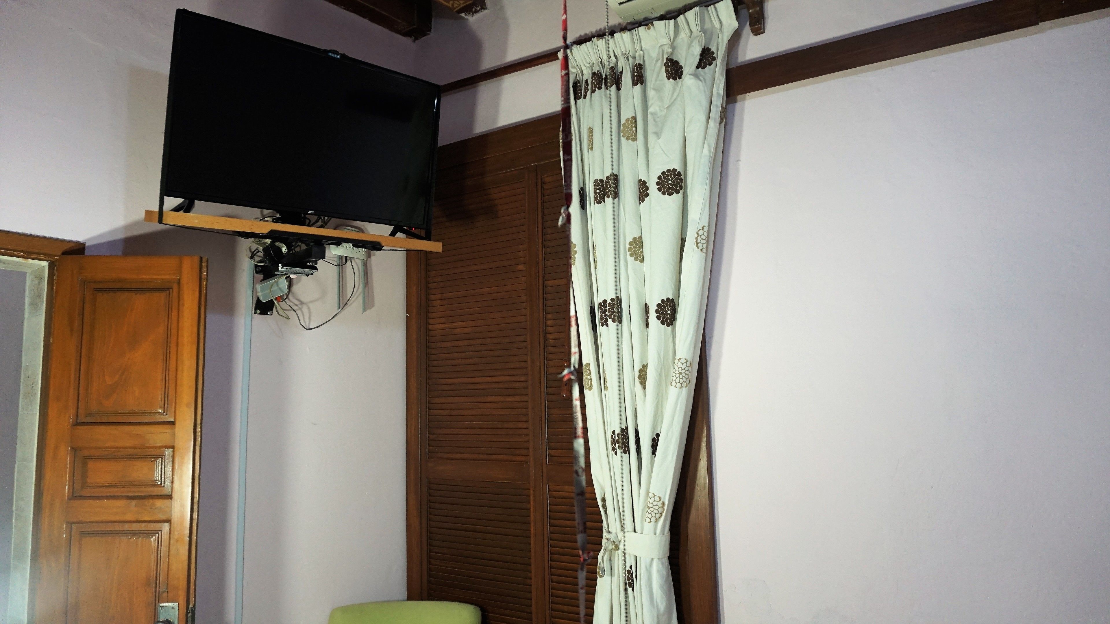 A room with a wooden door, a television mounted on the wall, and a curtain with a floral pattern.