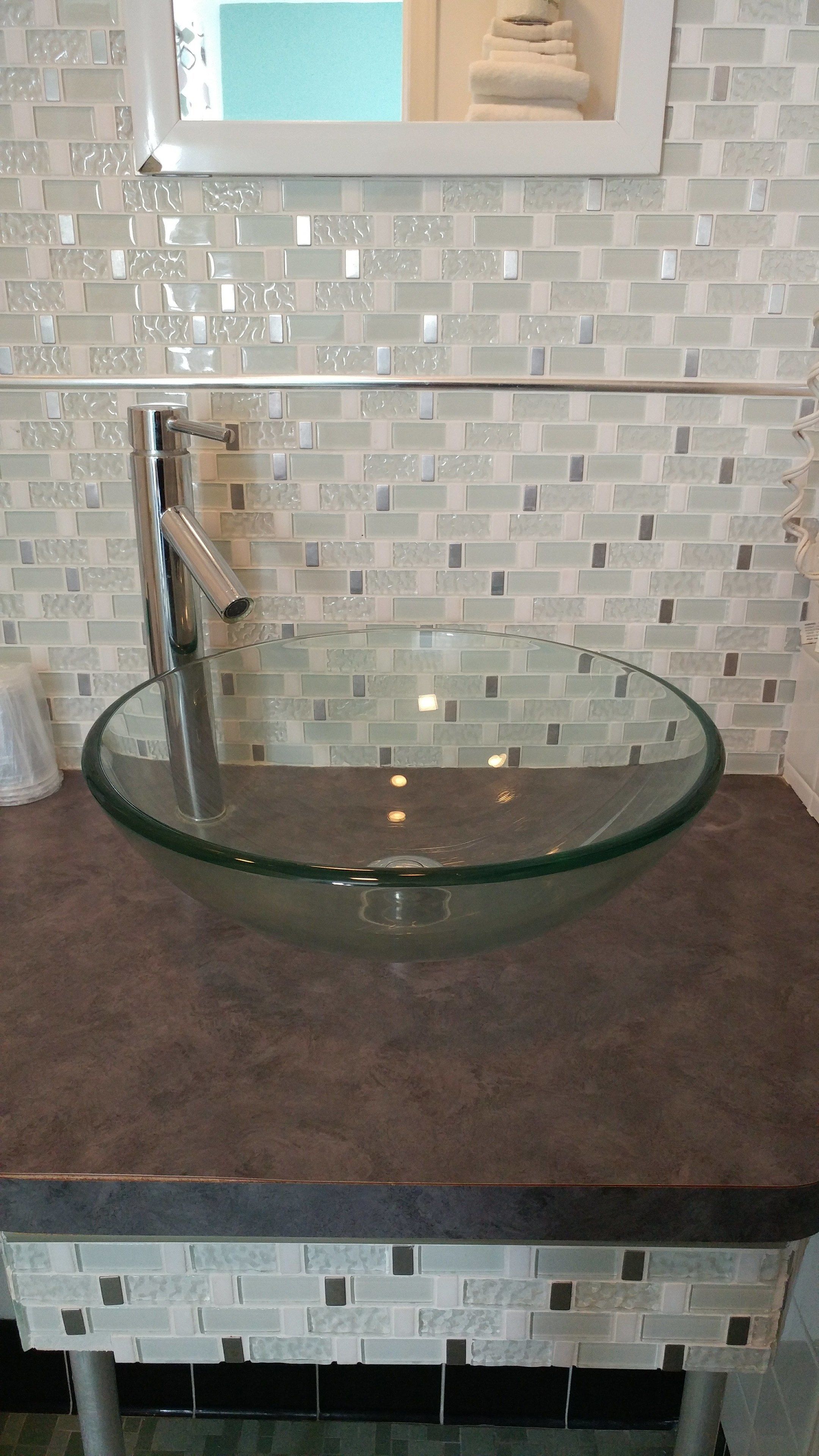 A bathroom with a glass bowl sink, a mirror above it, and a tiled backsplash.