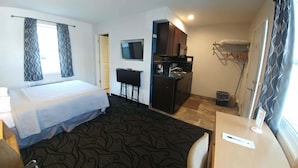 Une chambre d’hôtel comprenant un lit, un bureau avec un ordinateur, une télévision, une kitchenette et un espace douche.
