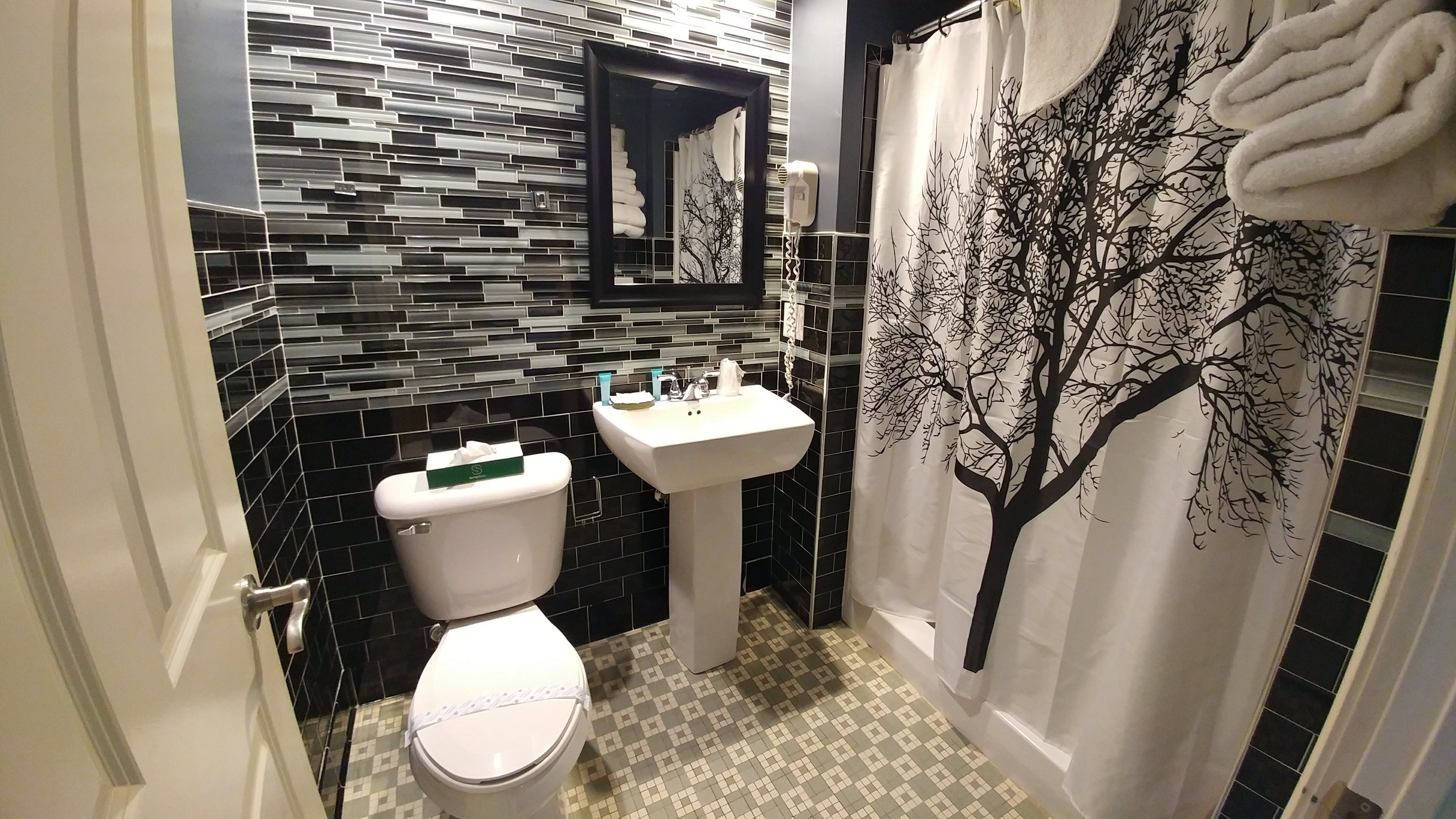 Un baño con inodoro, lavamanos y cortina de ducha con diseño de árbol.