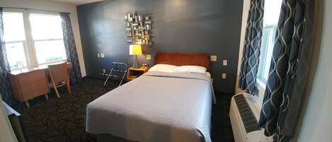 Una habitación de hotel con cama, escritorio, silla, lámpara y equipo de aire acondicionado.