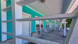 Un espace extérieur abrité, avec une rangée de chaises bleues et une porte blanche.