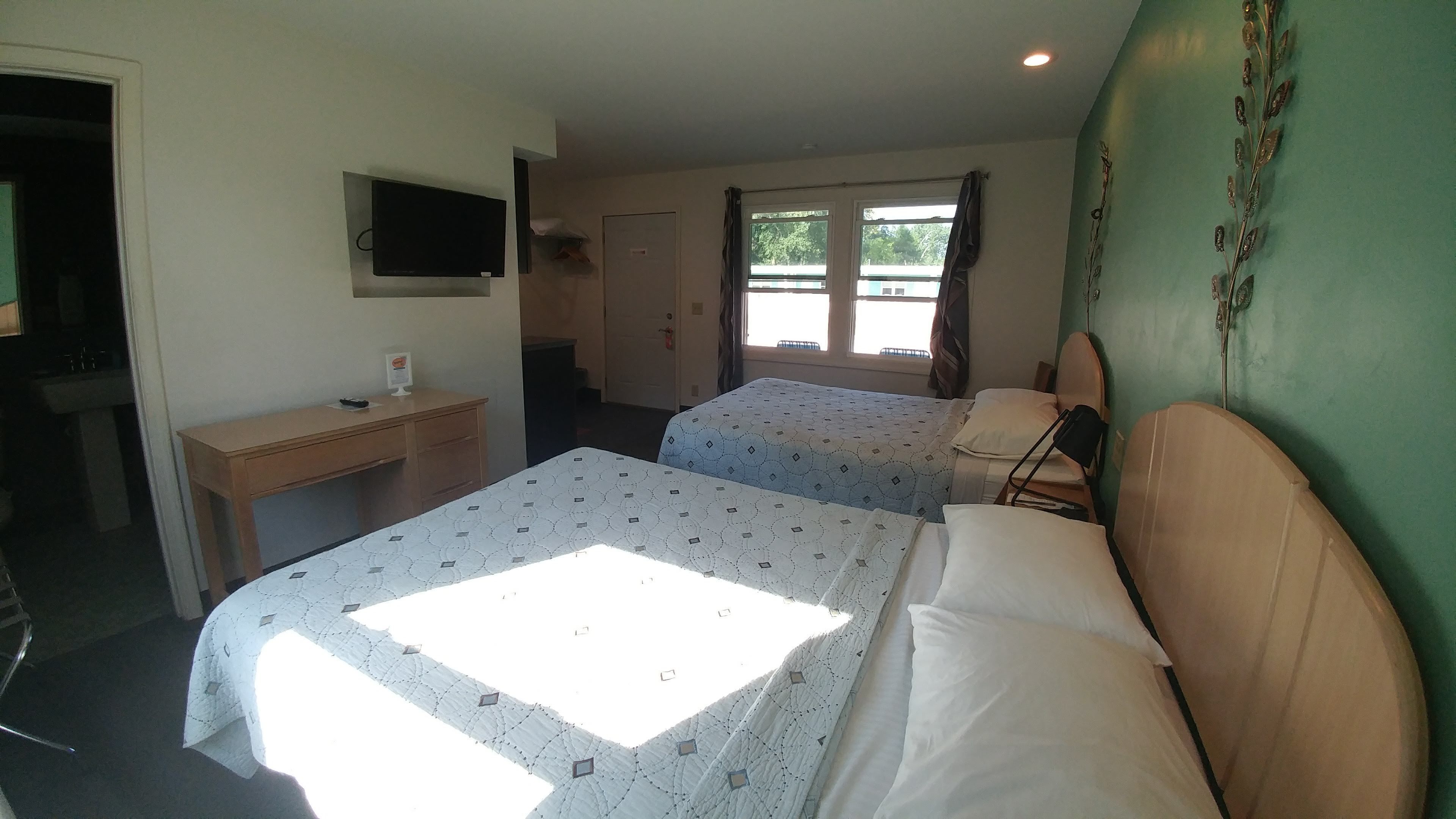 Habitación de hotel con dos camas, un escritorio, televisor y ventana con cortinas.
