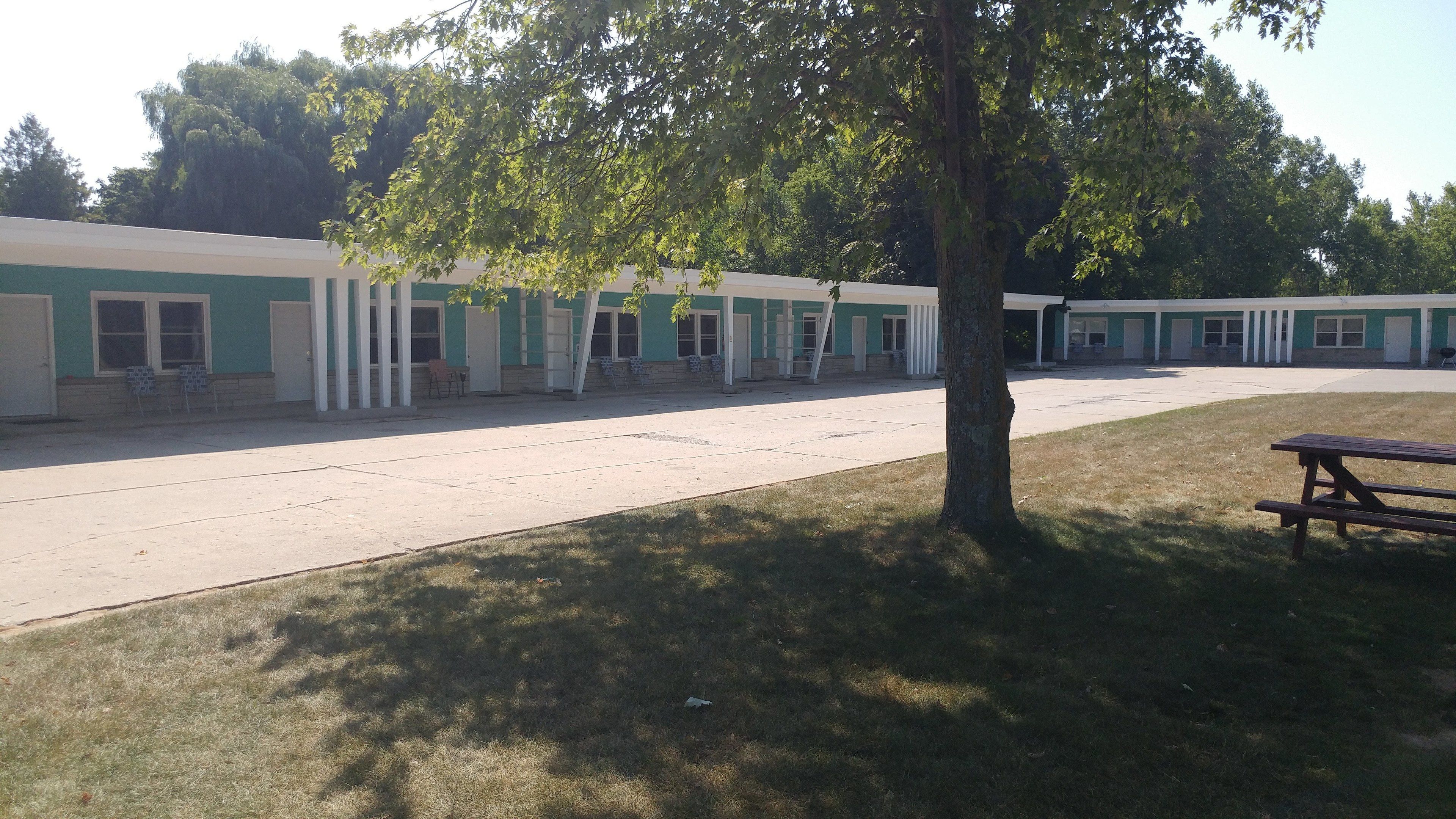 A row of motel-style buildings with a central parking area and a picnic table.