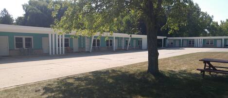 A row of motel-style buildings with a central parking area and a picnic table.