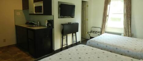 Une chambre d’hôtel équipée d’une kitchenette, d’une télévision, de deux lits et d’une fenêtre avec des rideaux.