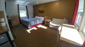 Una habitación de hotel con cama, sofá, mesita y ventana con cortinas.