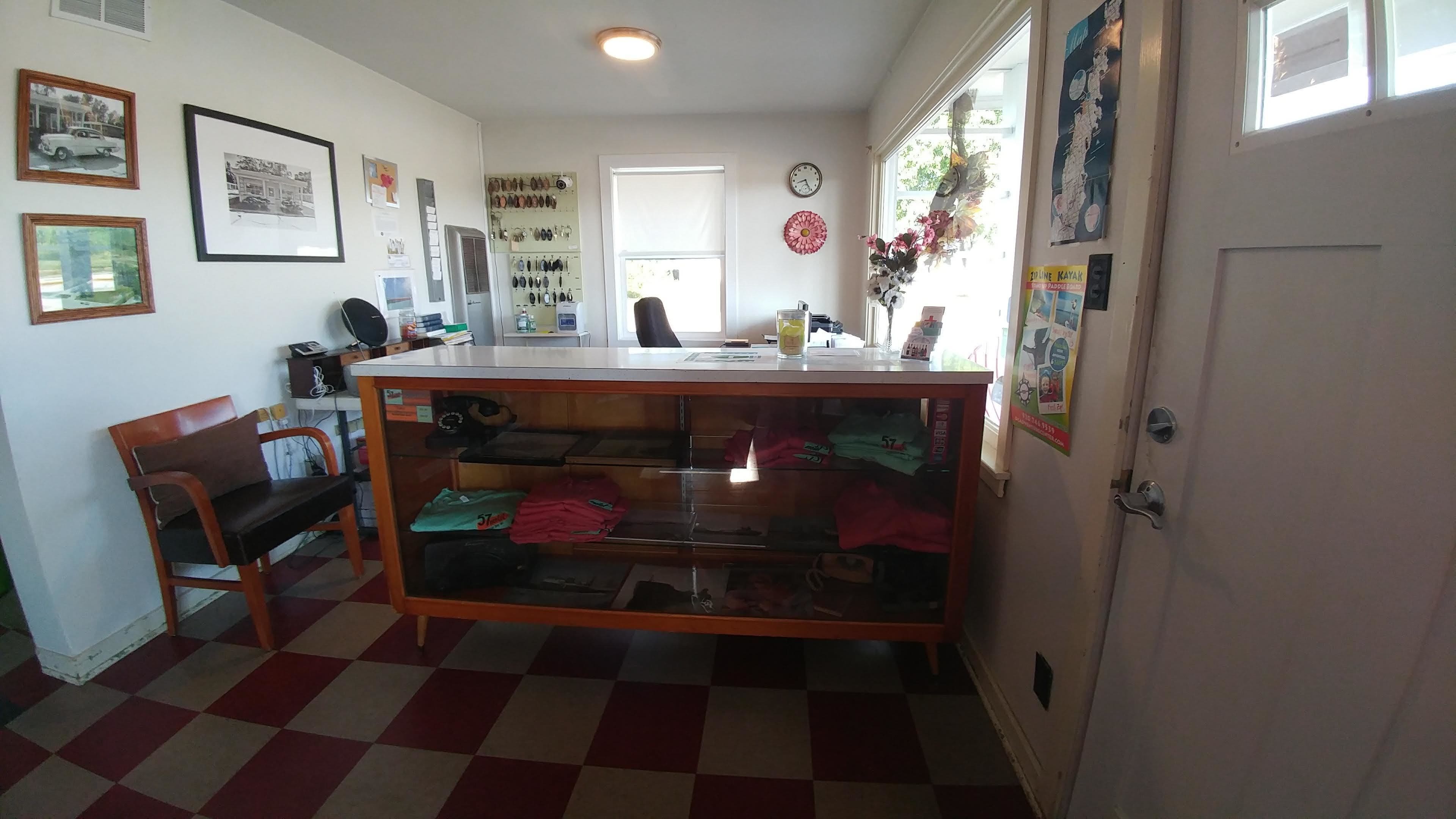 Een kamer met een zwart-wit geruite vloer, een houten bankje, een bureau met lades, en diverse voorwerpen aan de muur.