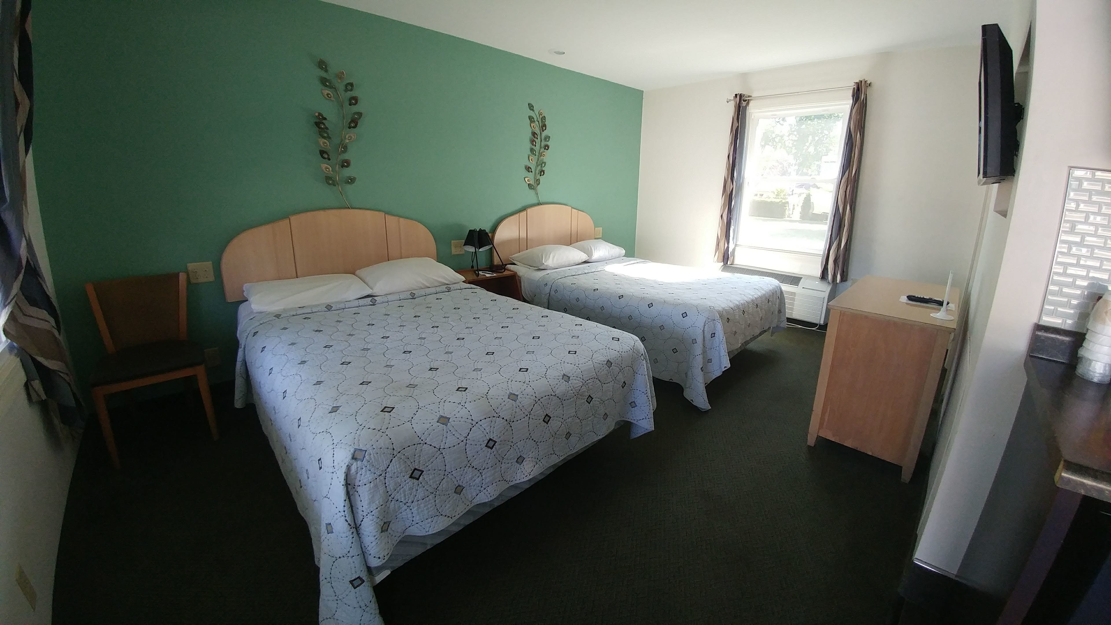 A hotel room with two beds, a wooden chair, a desk, a TV, and a window with curtains.