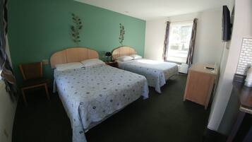 A hotel room with two beds, a wooden chair, a desk, a TV, and a window with curtains.