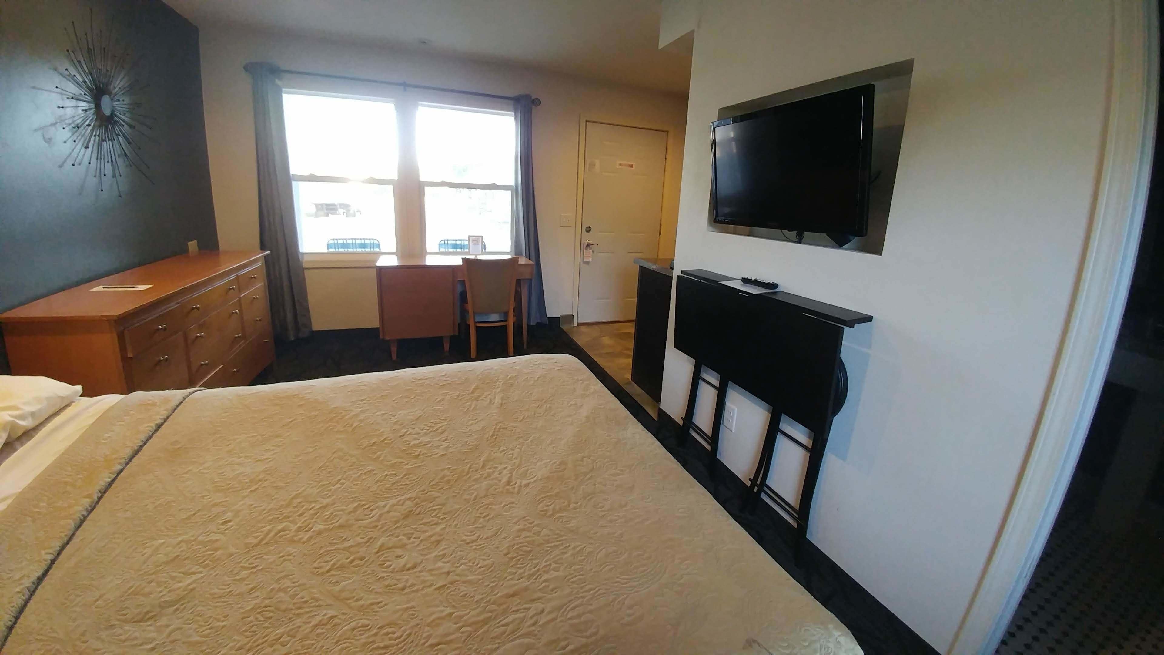 Una camera d'albergo con un letto, una scrivania, una sedia, una TV e un comò.