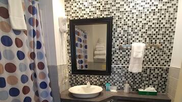 A bathroom with a white sink, a toilet, and a shower with a polka dot curtain. The walls are tiled with a mosaic pattern.