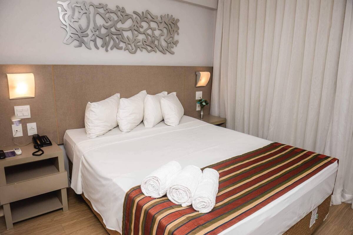 Una habitación de hotel con una cama grande, ropa de cama blanca, una manta de diseño a rayas y un elemento decorativo en la pared.