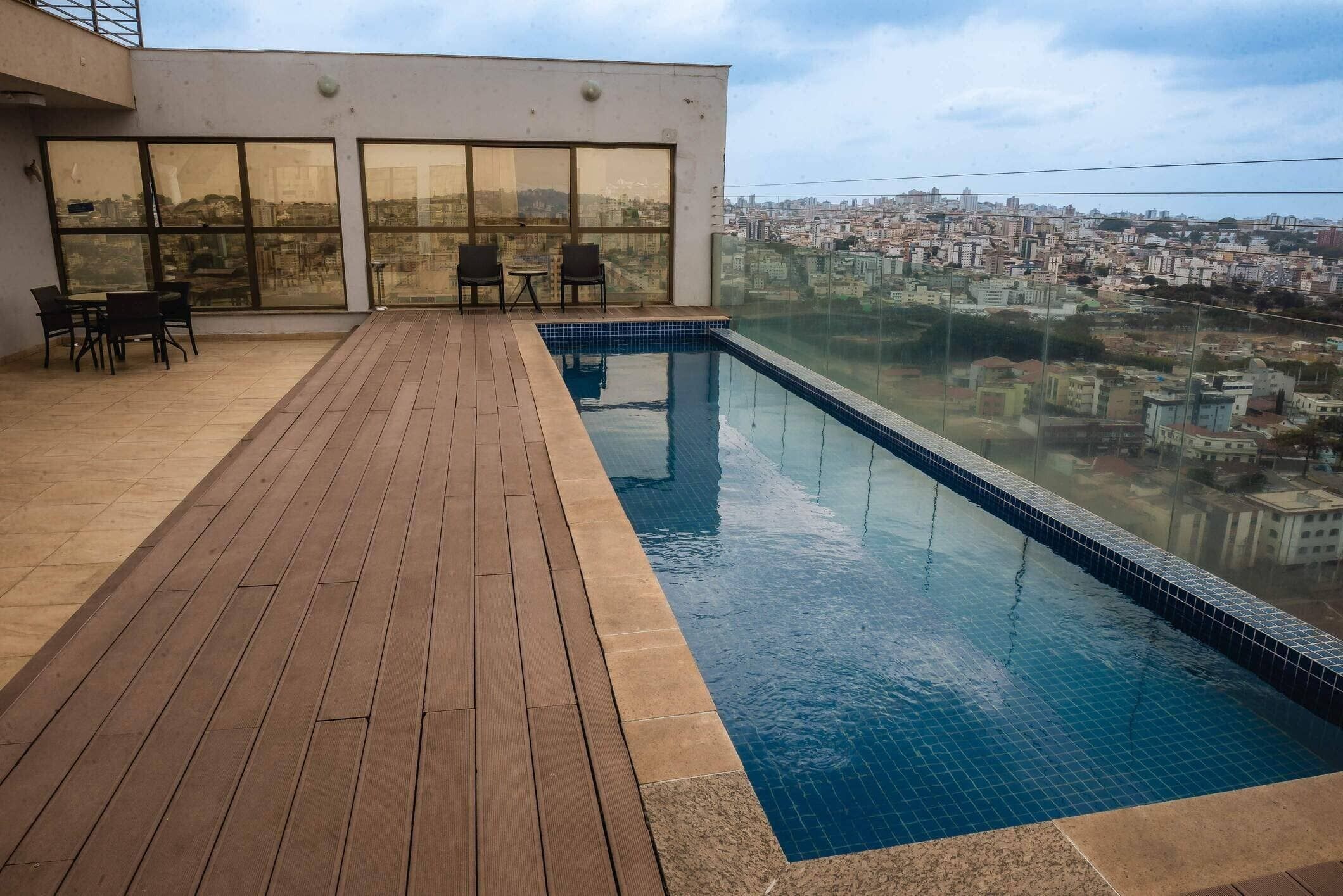 Una piscina en la azotea con terraza de madera, grandes ventanales y vistas panorámicas de la ciudad.