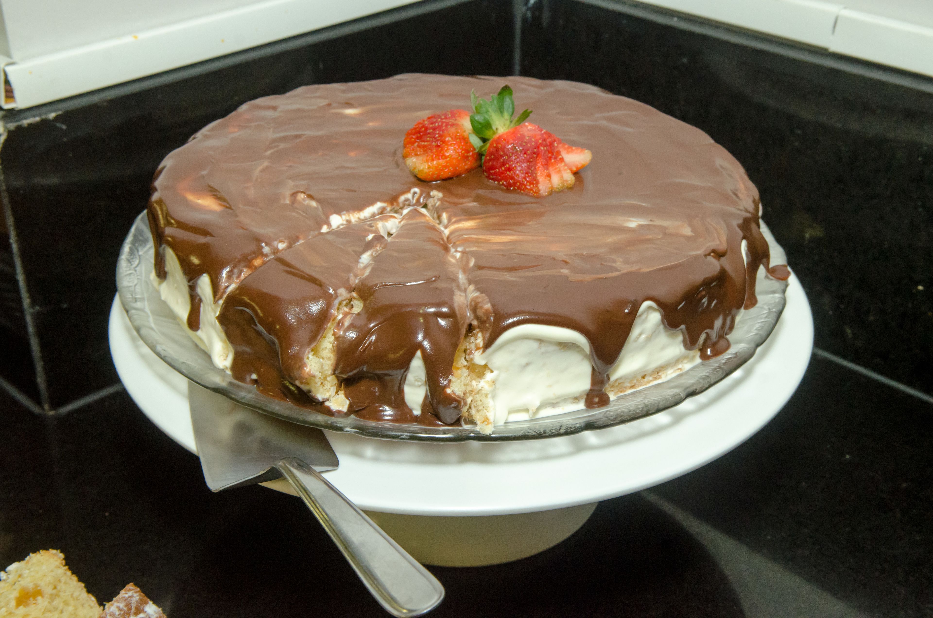 A cake with chocolate glaze and strawberries on a glass cake stand.