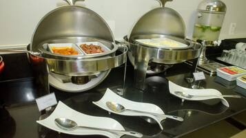 Disposición de un bufé con recipientes cubiertos para alimentos y utensilios de servicio sobre una encimera negra.