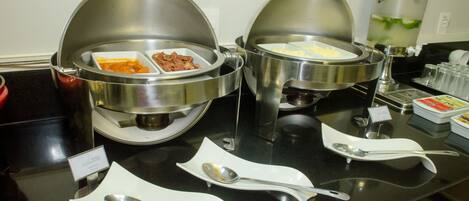 Disposición de un bufé con recipientes cubiertos para alimentos y utensilios de servicio sobre una encimera negra.