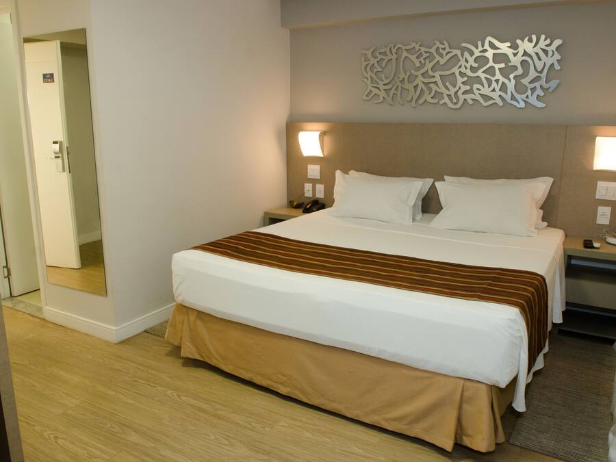 Habitació d'hotel amb un llit gran, dues taules de nit, un taulell i un element decoratiu a la paret.