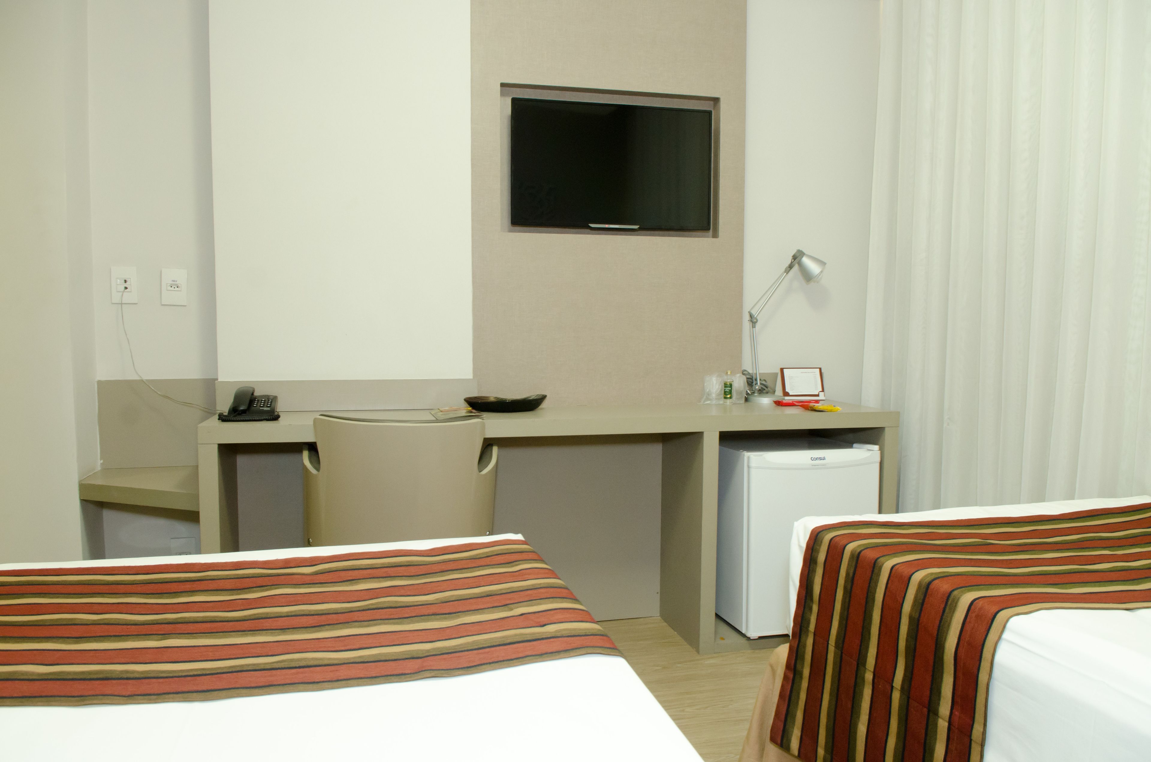 Une chambre d’hôtel avec deux lits, un bureau équipé d’une télévision, d’une lampe, d’un téléphone et d’un petit réfrigérateur.