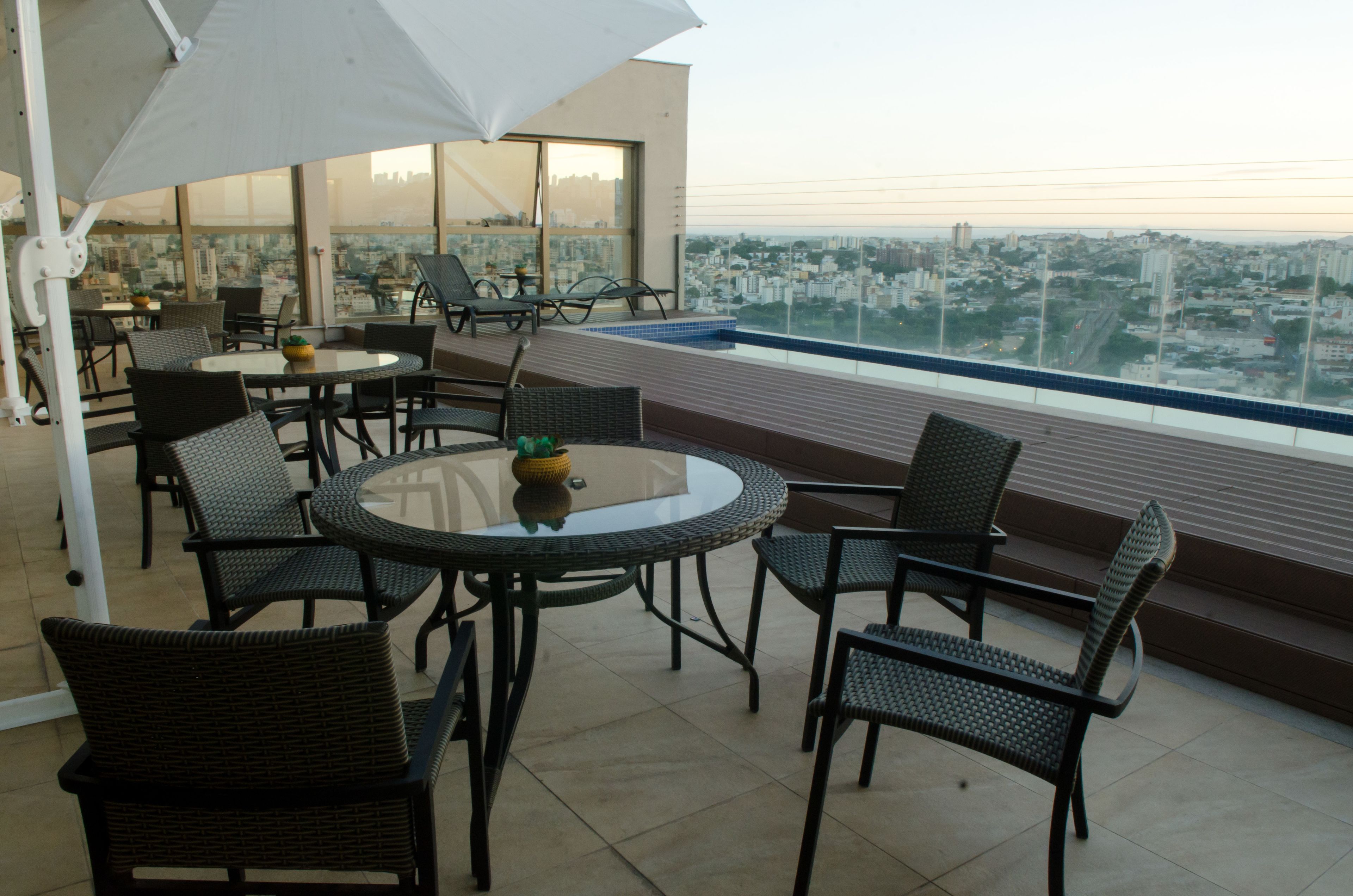 A rooftop terrace with round tables and chairs, a large umbrella, and a city view.