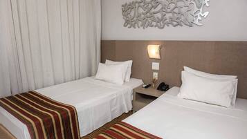 A hotel room with two beds, a striped blanket on one bed, a wall-mounted light, and a decorative wall piece.