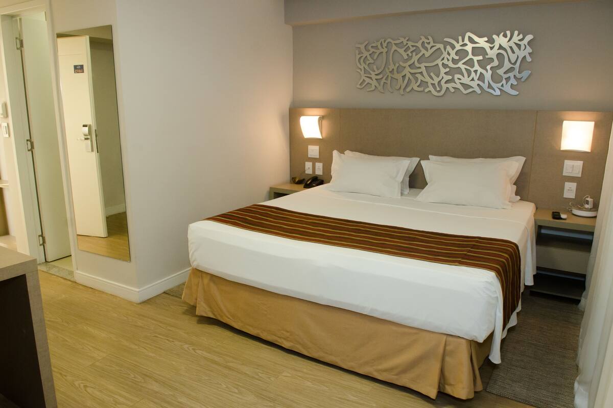 Una habitación de hotel con una cama grande, mesitas de noche, un espejo y un adorno en la pared.