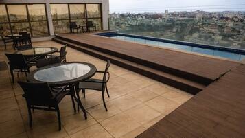 A rooftop terrace with a pool, outdoor seating, and a city view.