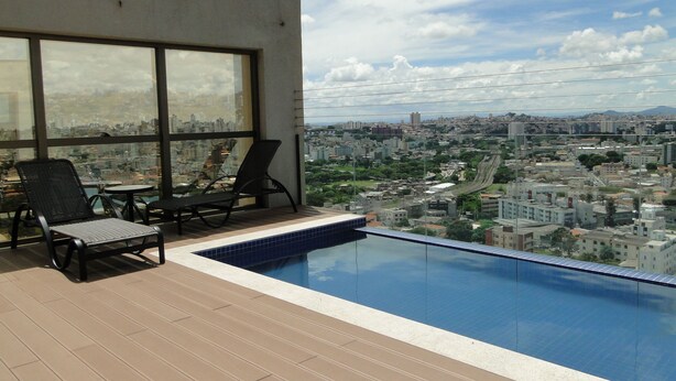 Área de piscina en la azotea con sillones y vista panorámica de la ciudad.