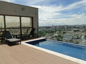Área de piscina en la azotea con sillones y vista panorámica de la ciudad.