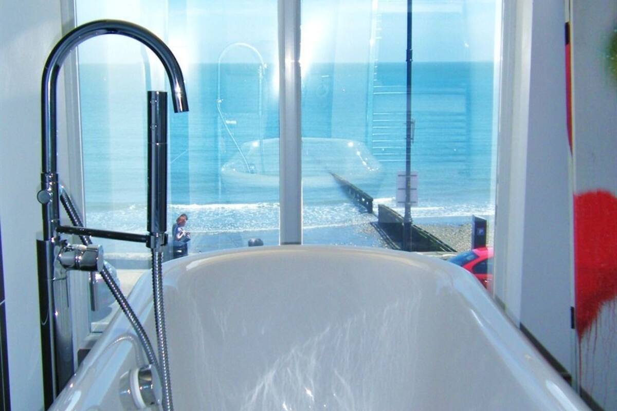Un baño con bañera, ducha y ventana con vistas al mar.