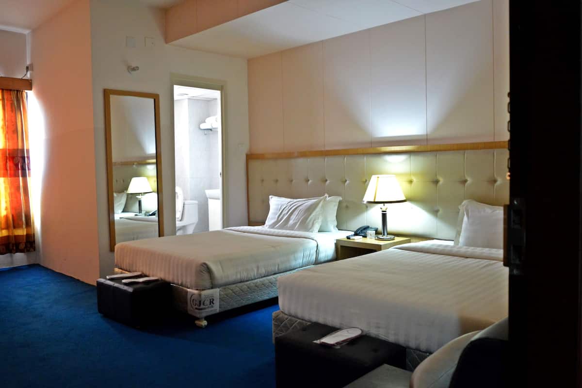 Ein Hotelzimmer mit zwei Betten, einem Nachttisch mit Lampe, einem Koffer und einem Spiegel an der Wand.