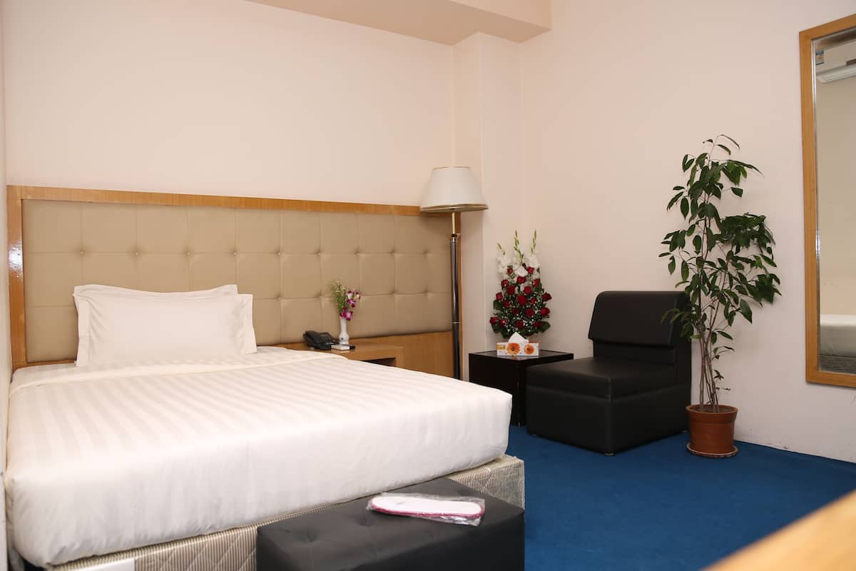 Ein Hotelzimmer mit einem großen Bett, einem Nachttisch mit Lampe, einem Sessel, einer Topfpflanze und einem kleinen Tisch mit Blumen.