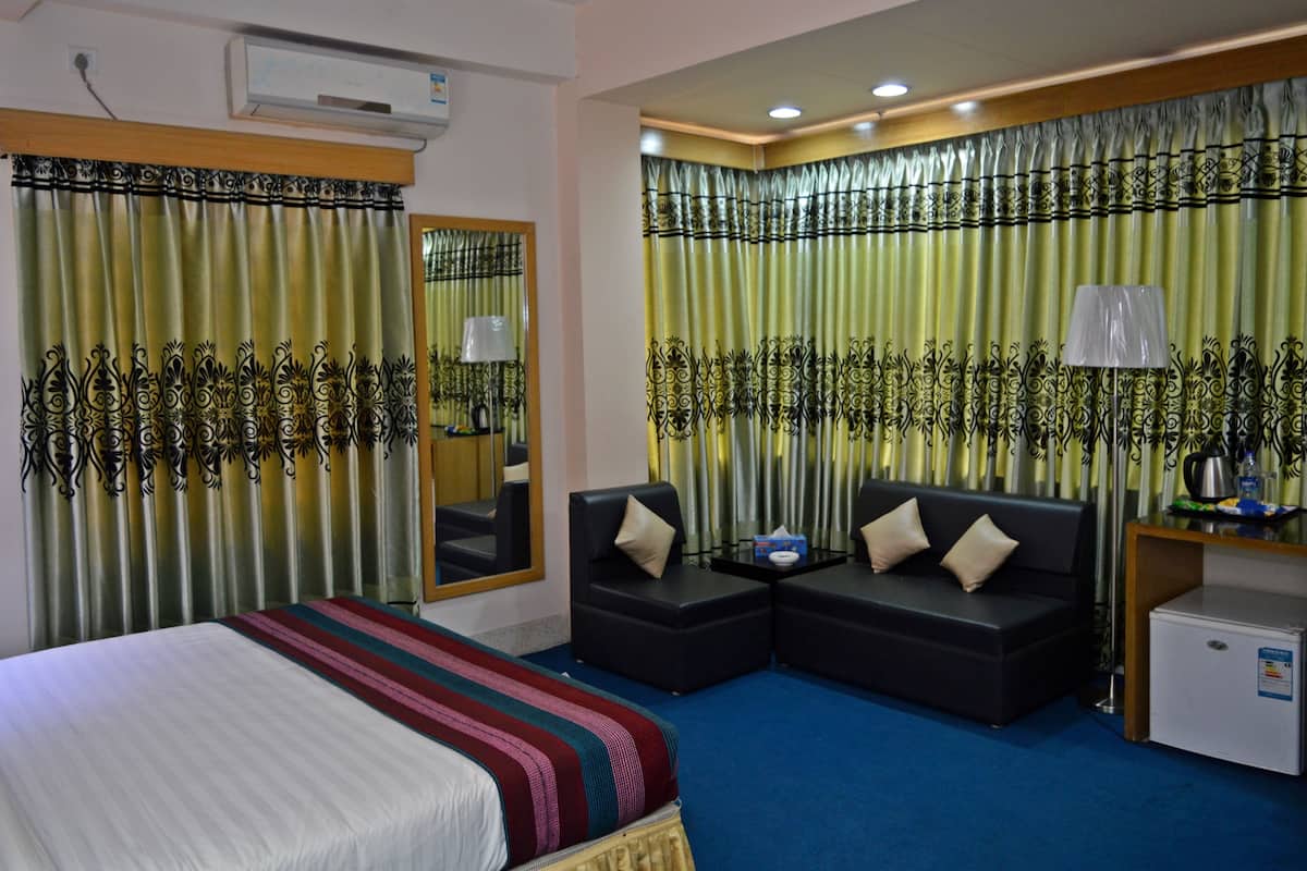 Ein Hotelzimmer mit einem Bett, zwei Sofas, einem kleinen Tisch, einem Kühlschrank und Vorhängen mit dekorativem Muster.
