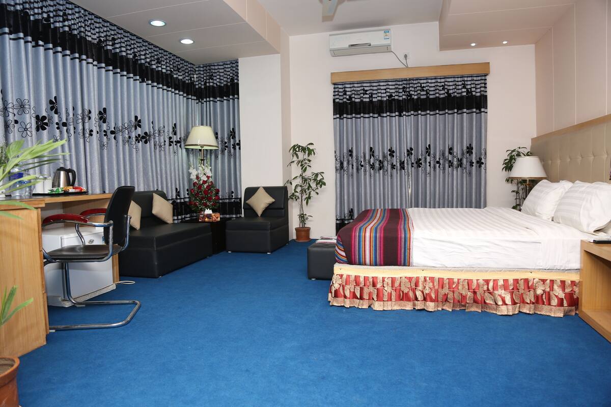 Ein Hotelzimmer mit Bett, Schreibtisch, Sessel, Sofa und einer Zimmerpflanze.